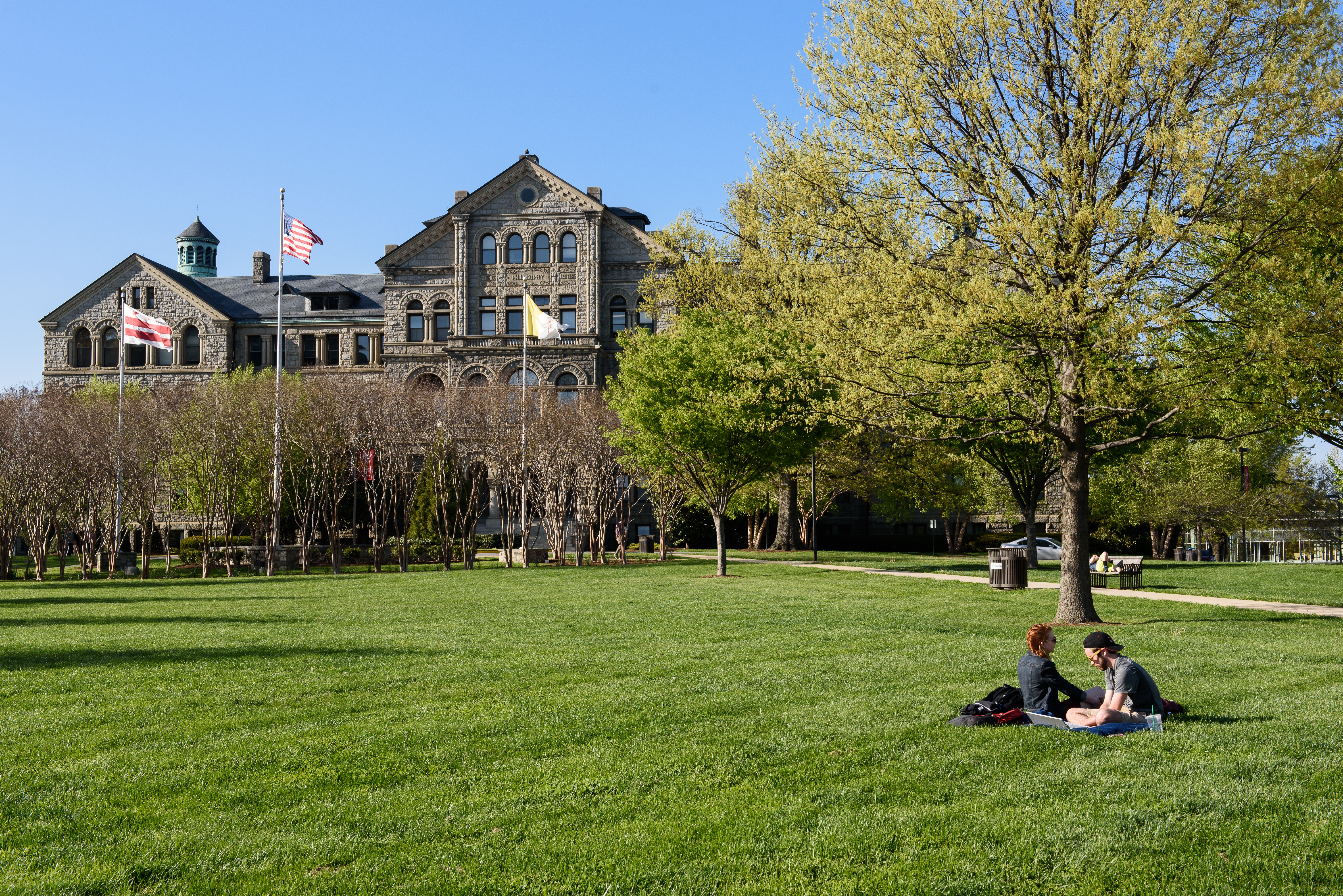 University Lawn Facing McMahon Hall, green leaves on trees and green grass.  Students studying on the Lawn